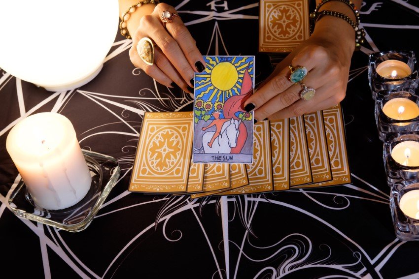 Woman Wearing Several Beautiful Rings Has Tarot Spread On Table And Holds The Sun Card In Relation To Evolution Of Tarot Reading