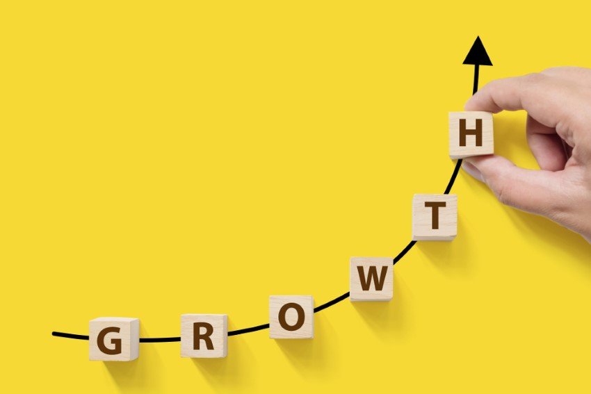 Wooden Blocks That Make Up The Word Growth Laid Out On A Curving Black Arrow Pointing Upwards Symbolizing Personal Growth